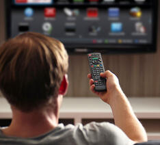 Mand bruger fjernbetjening foran fjernsynet 