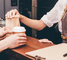 En medarbejder på en cafe betjener en kunde og sælger ham en kaffe og noget sødt til 