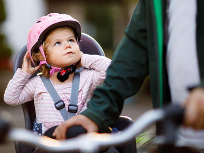 Lille pige sidder i cykelstol med cykelhjelm på