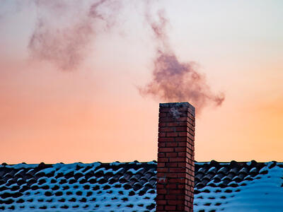 Røg kommer ud af skorsten en kold vinterdag med sne på taget af huset