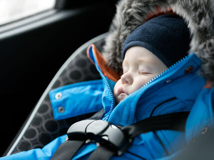 Baby sover med flyverdragt på i autostol
