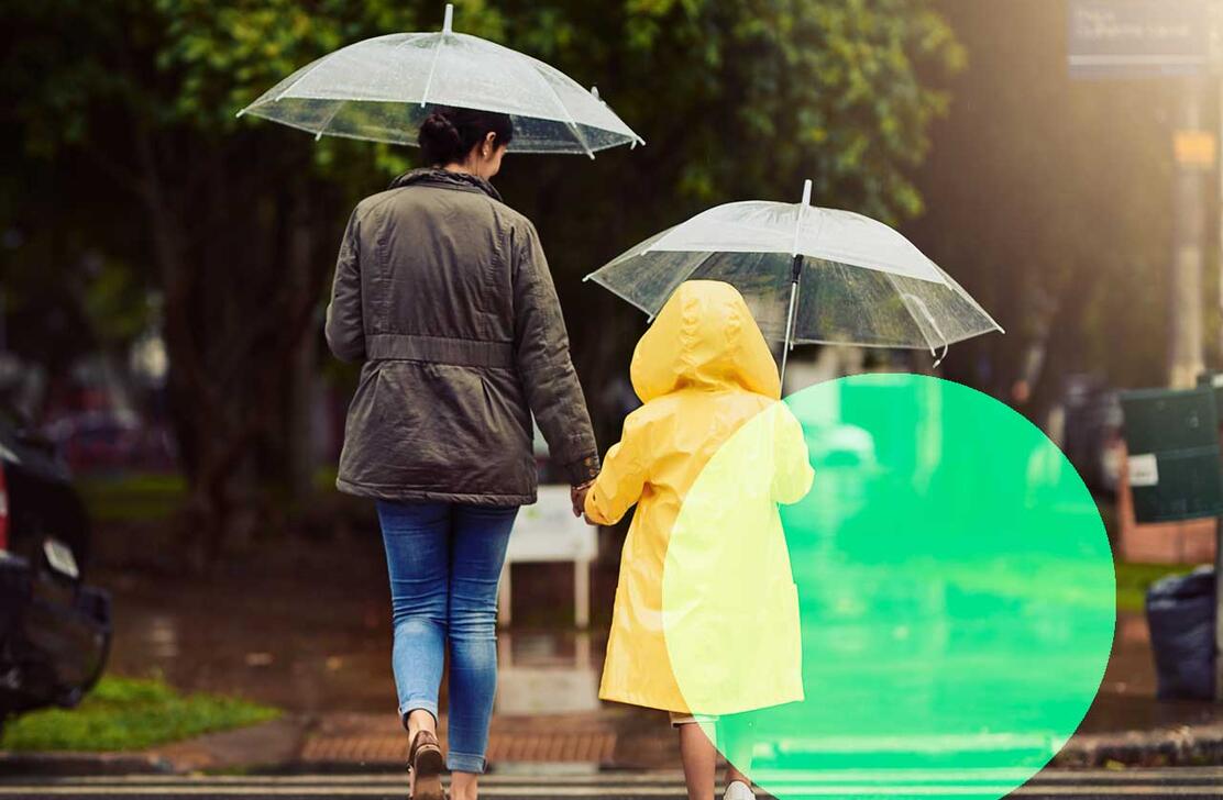Kvinde går med sit barn i regnvejr iført regntøj med paraply
