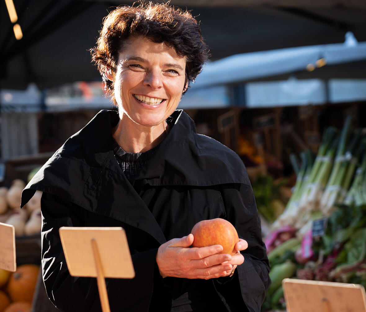 Anja Philip står med et æble på et udendørs marked, kigger ind i kameraet og smiler