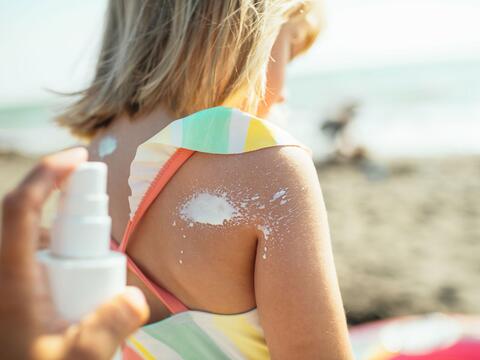 Solcreme bliver sprayet på ryggen af et barn