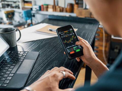 Mand med telefon og computer kigger på investeringer og aktiesparekonti
