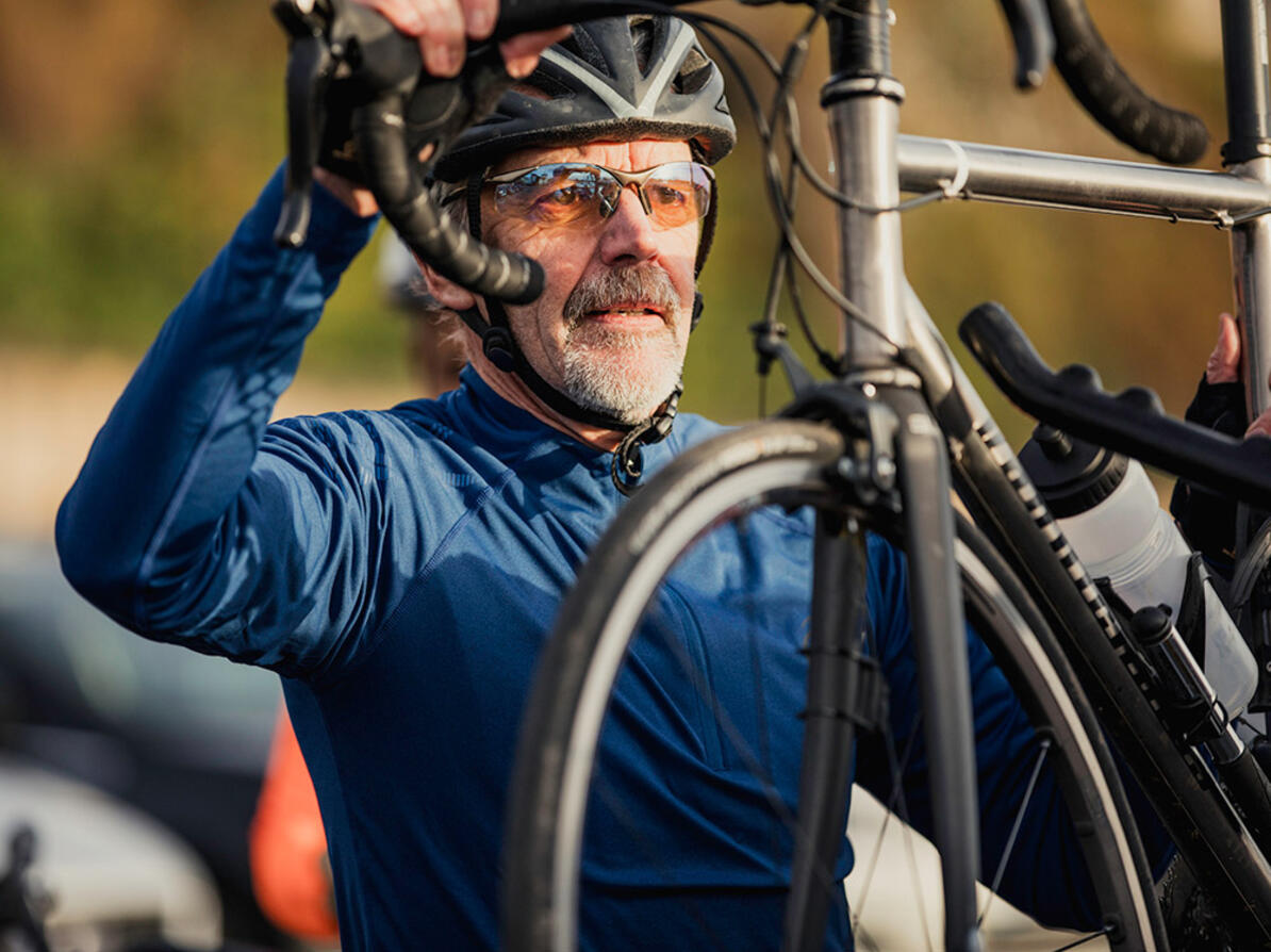 Mand i cykeltøj og cykelhjelm sætter cykel på holder på bilen