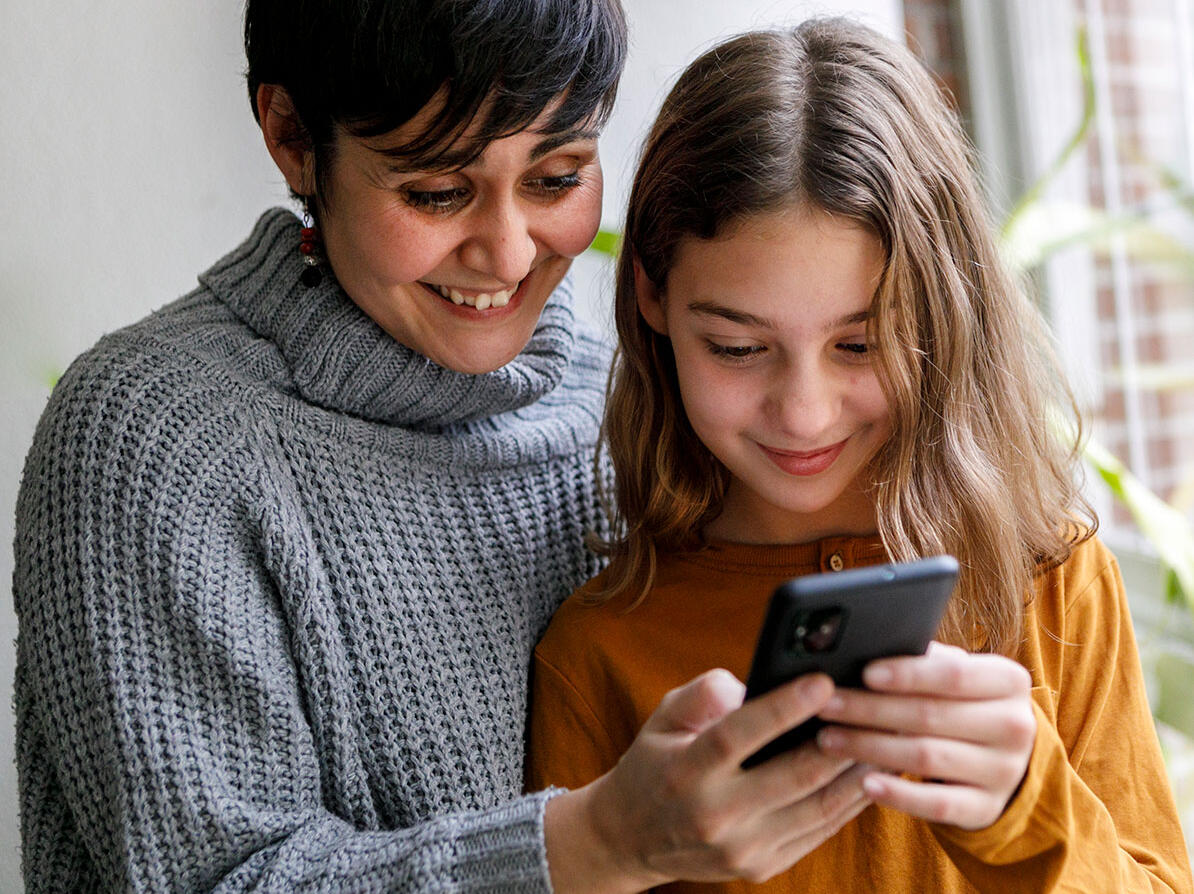 mor og datter står og kigger på smartphone, de skal beskytte datterens telefonnummer for telefonsalg