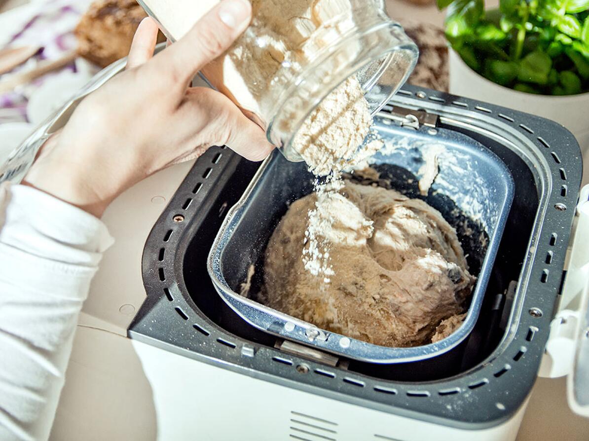 Person hælder ingredienser i en bagemaskine