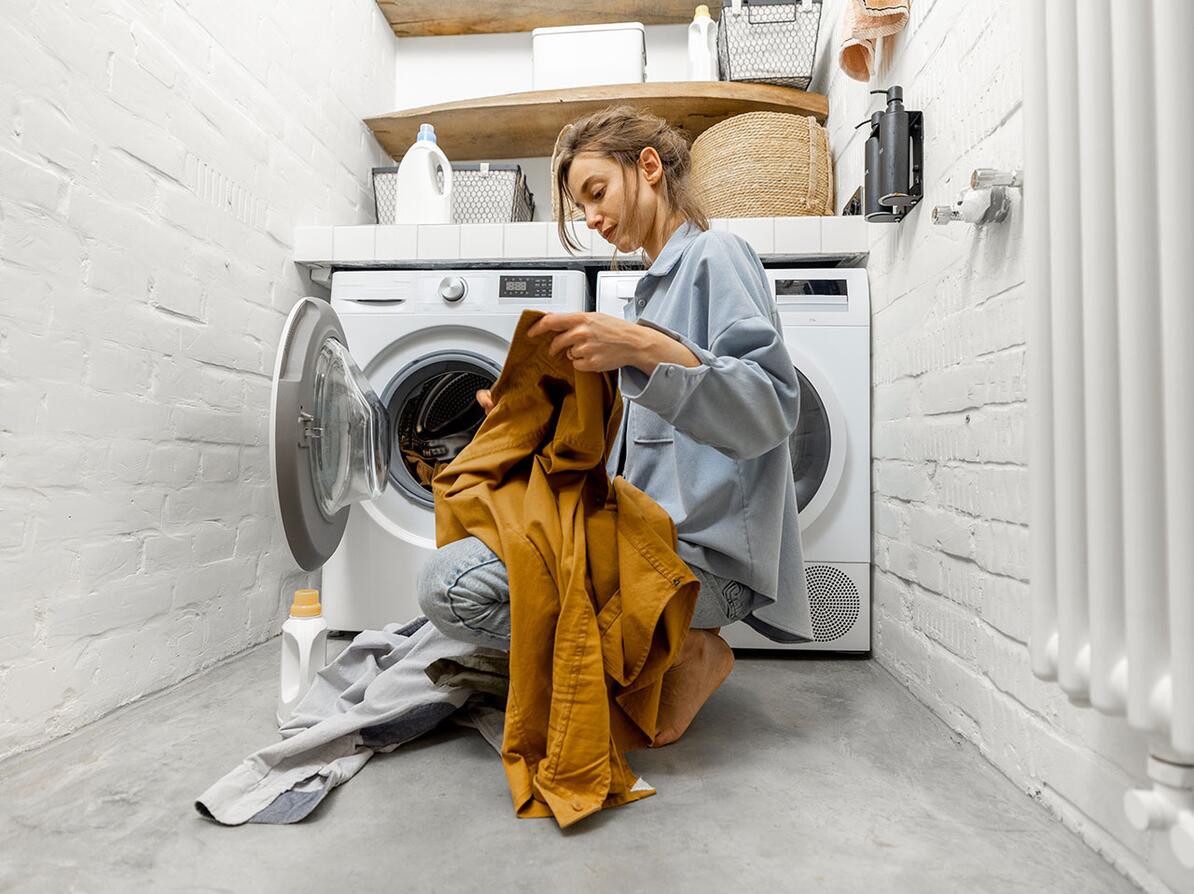 Kvinde sidder med noget tøj ved en vaskemaskine