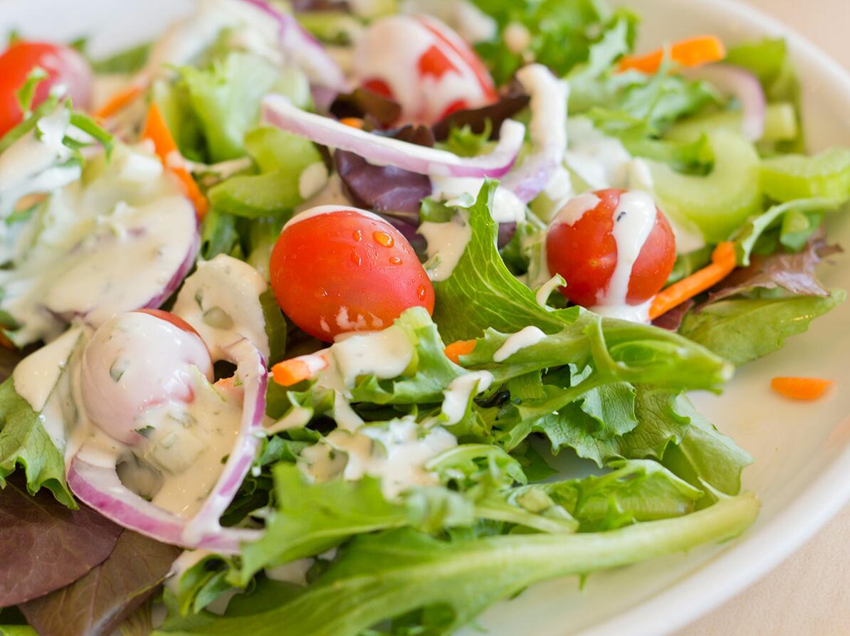 Salat med cherrytomater, gulerod, rødløg og en masse dressing på en tallerken. 