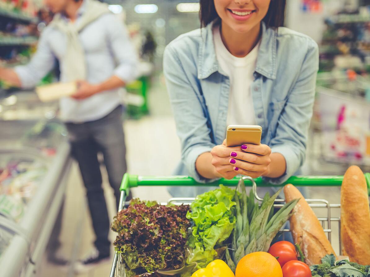 kvinde på indkøb i supermarked med indkøbsliste på mobilen. 