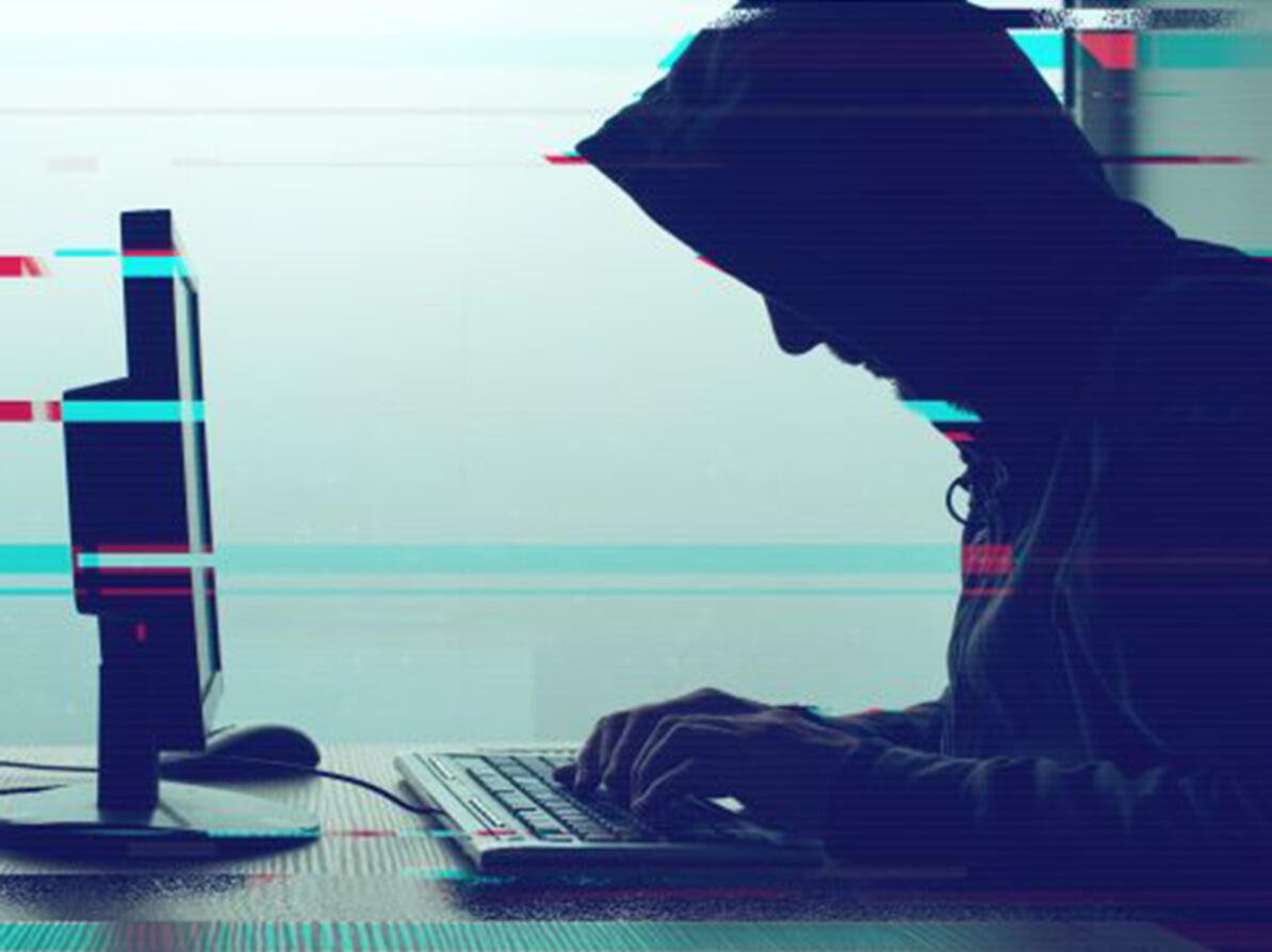 Person sidder med hætte på foran en computer