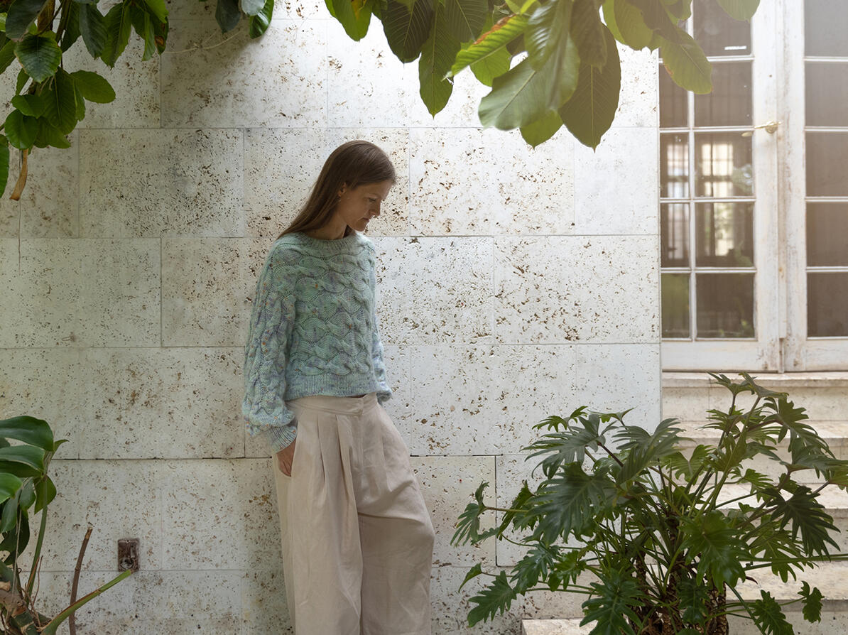 Kvinde i hørbukser og uldsweater står blandt grønne planter