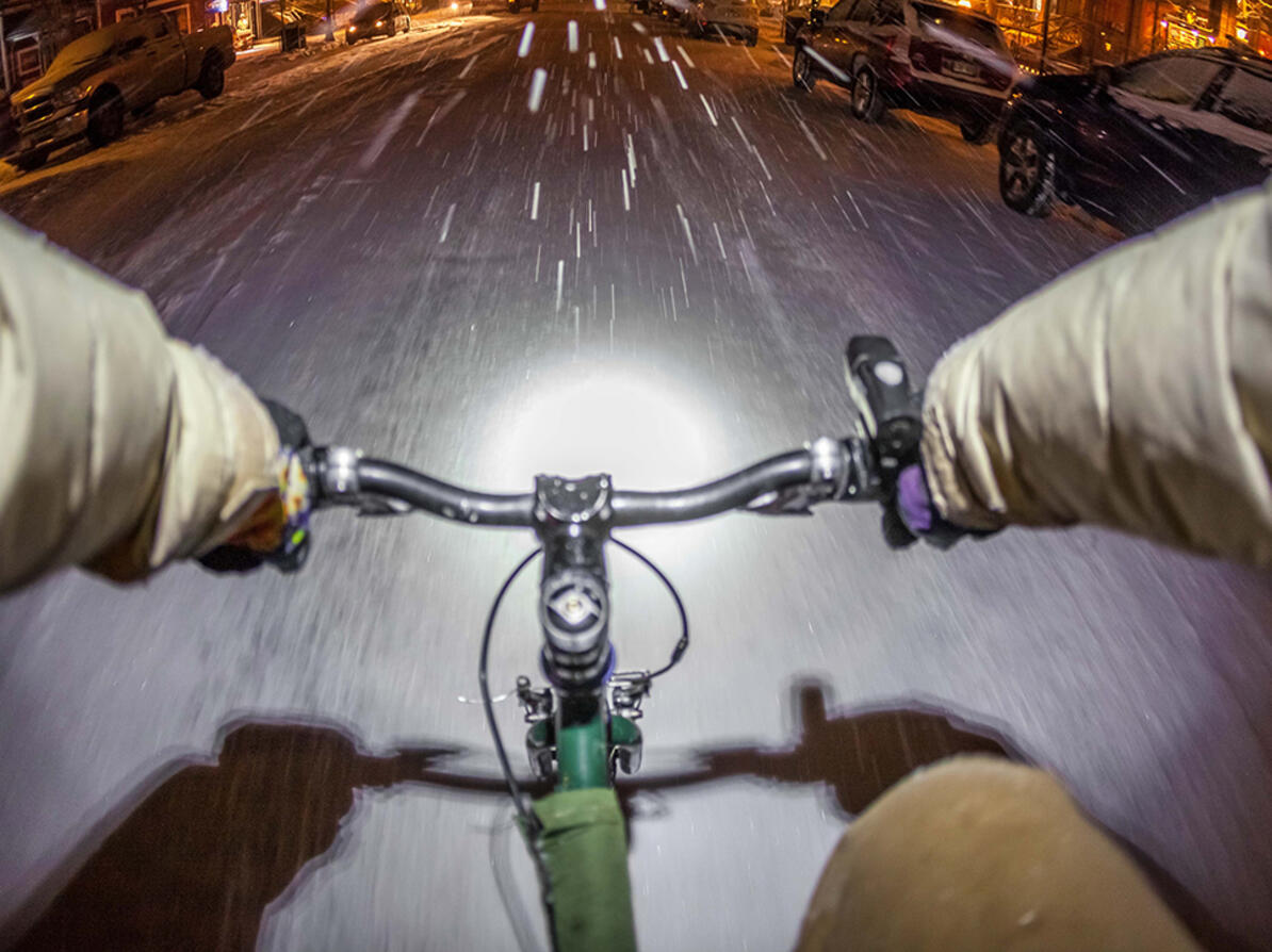 Person cykler udenfor i snevejr med tændte cykellygter med batterier
