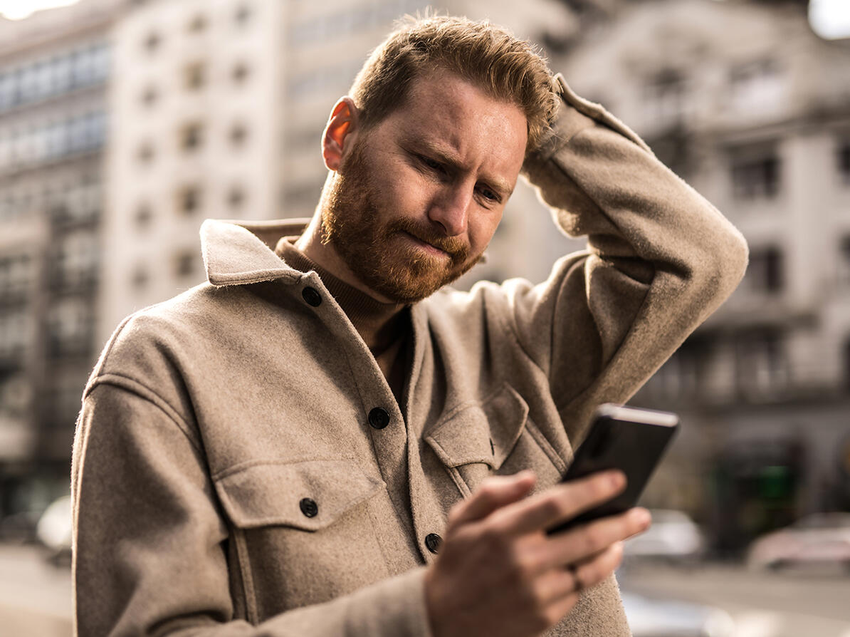 Mand klør sig i håret mens han kigger på sin smarthphone 