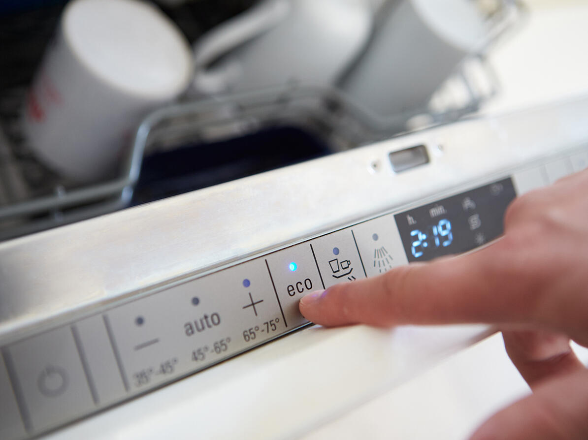 finger trykker på knap med eco-program på en fyldt opvaskemaskine