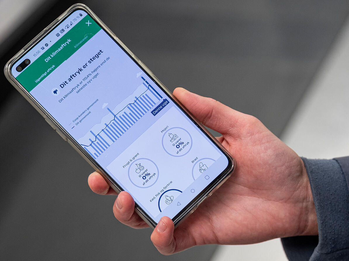 Hånd holder telefon med app der viser klimaaftryk fra madindkøb