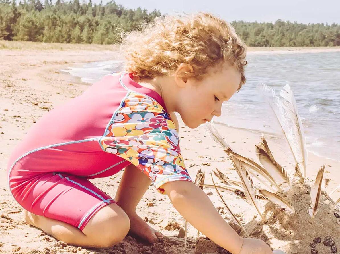 Barn med soltøj sidder i sand ved havet.