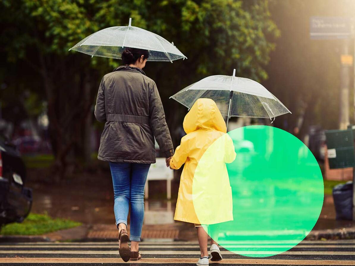 Kvinde går med sit barn i regnvejr iført regntøj med paraply