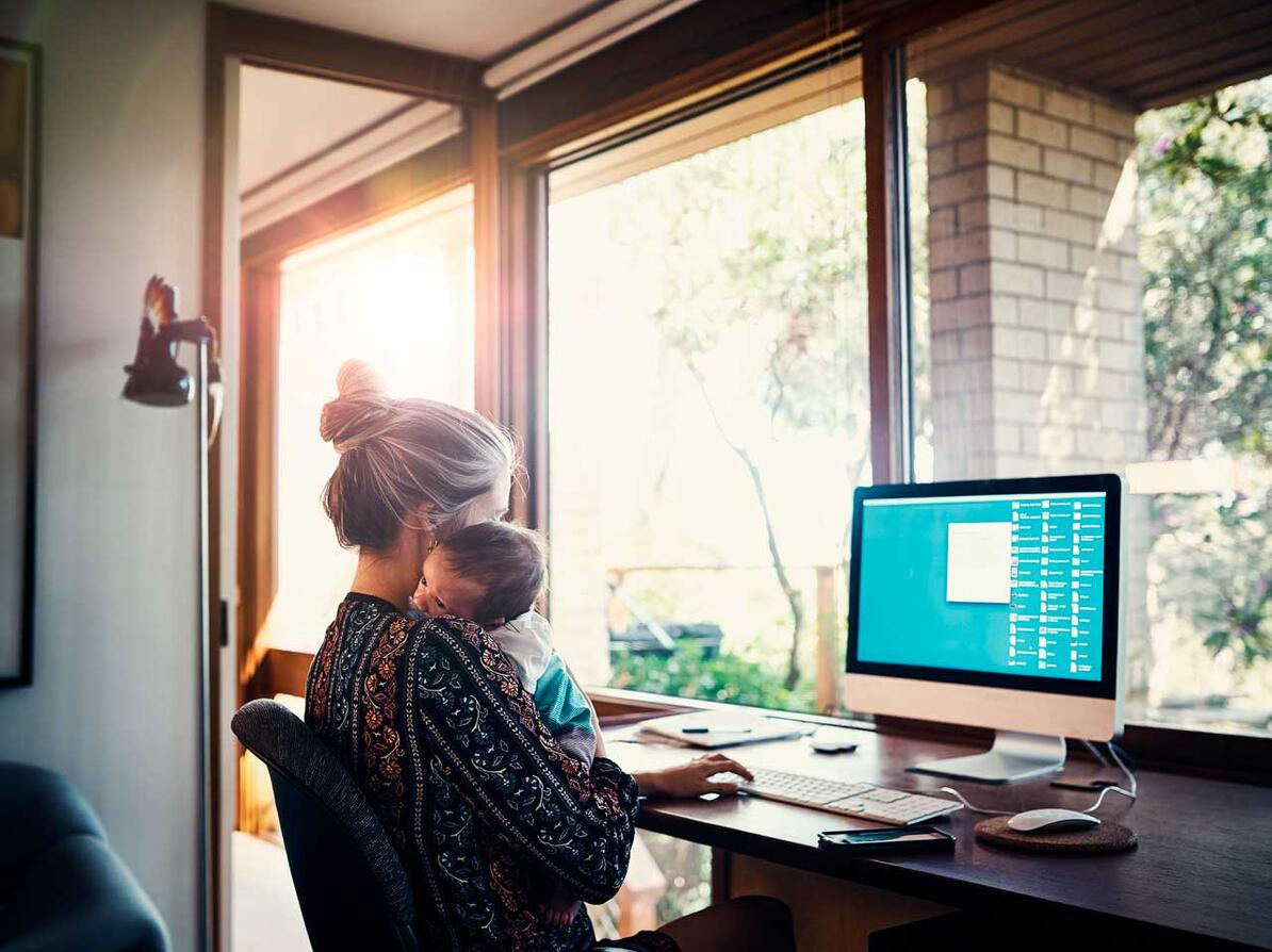 Kvinde sidder ved computeren med sit lille barn