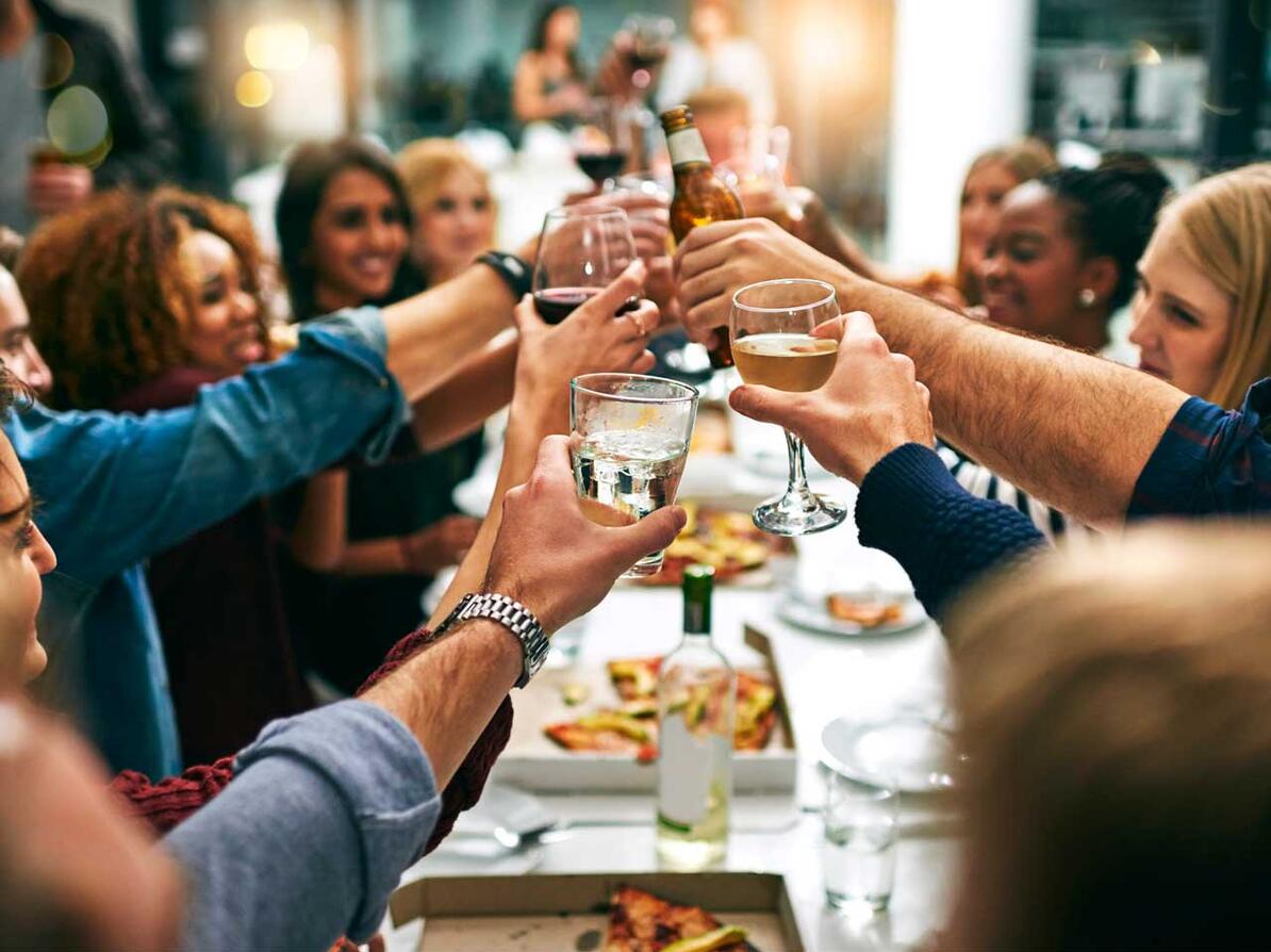 venner og familie spiser middag sammen og skåler i vinglas