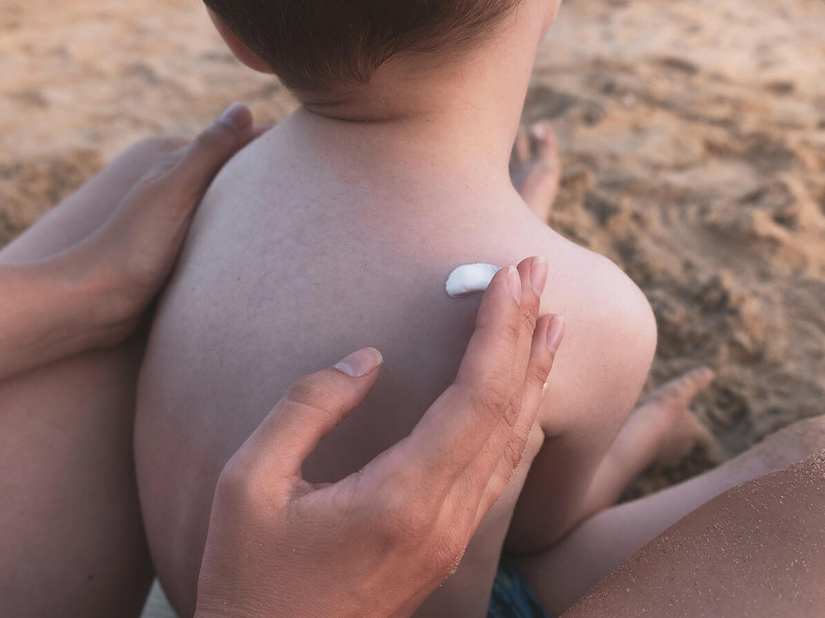 hånd smører solcreme på barneryg på stranden