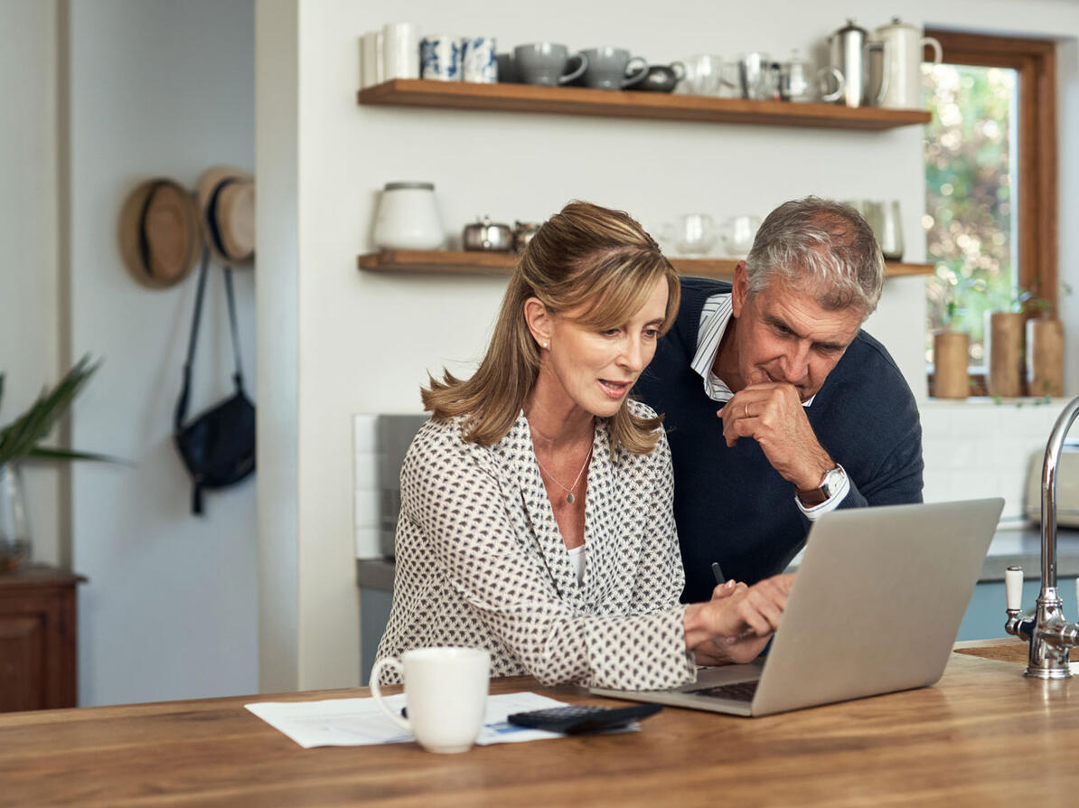 Kvinde viser sin mand en oversigt over pensioner på computer i køkken