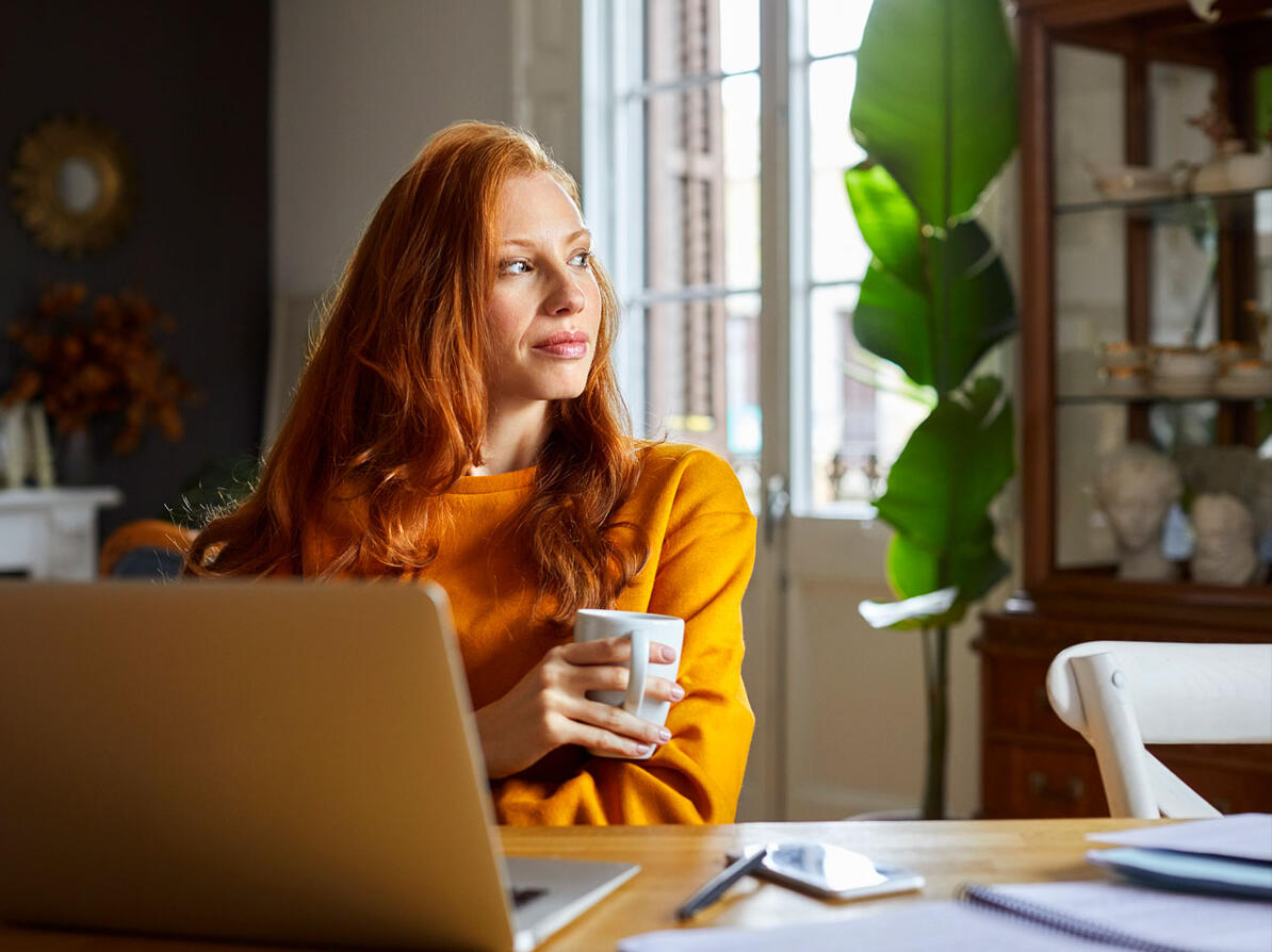 Kvinde ved sin computer kigger ud ad vinduet