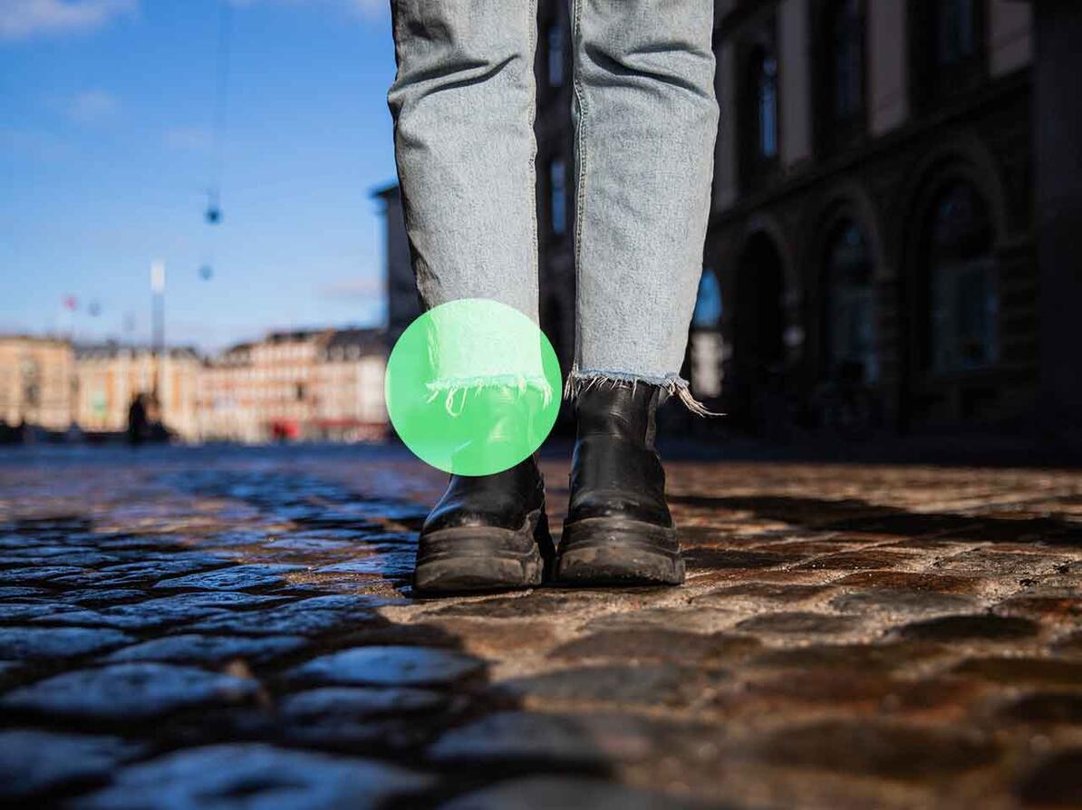 Ben med jeans og fødder med sko står på brosten