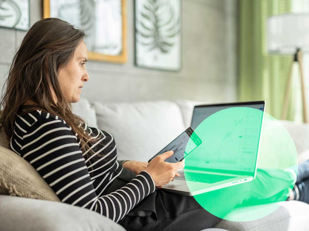 Kvinde med computer og mobil i sofa kigger på sine investeringer