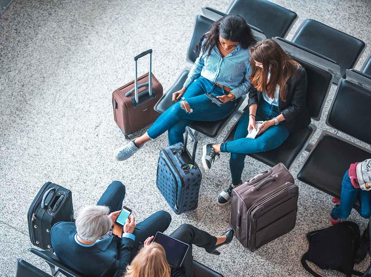 Gruppe af mennesker der sidder med deres bagage og venter i en lufthavn.