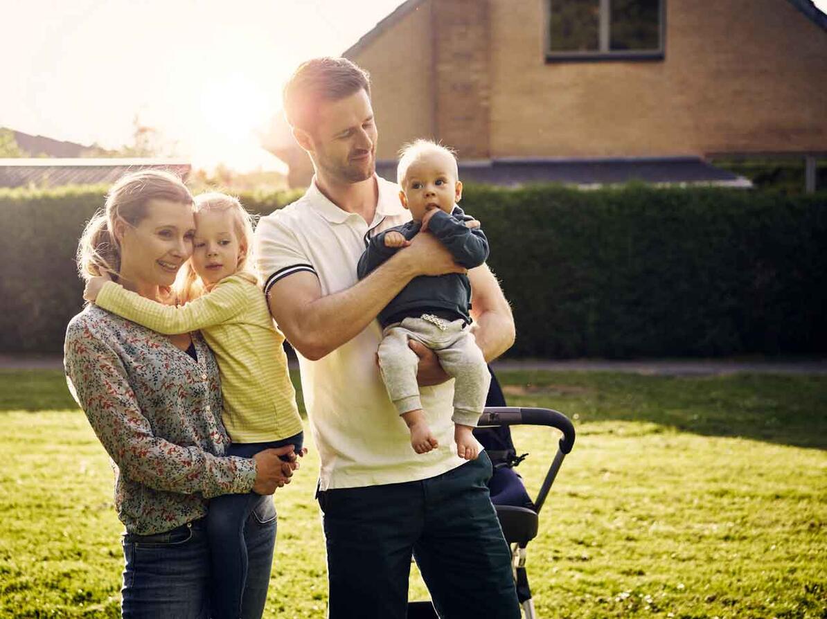 Kvinde og mand med to børn står i haven og kigger på deres nye hus