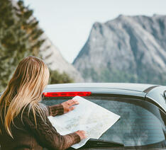 Kvinde med med vejkort og en udlejningsbil ved nogle bjerge