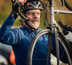 Mand i cykeltøj og cykelhjelm sætter cykel på holder på bilen
