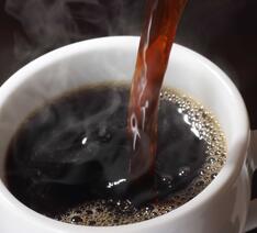 Sort, vellavet kaffe skænkes op i hvid kaffekop.