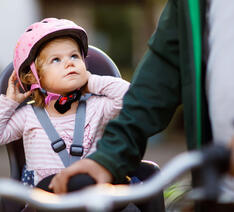 Lille pige sidder i cykelstol med cykelhjelm på