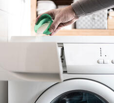 Person er ved at hælde vaskepulver i vaskemaskinen