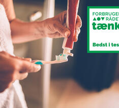 Kvinde putter tandpasta på tandbørste, foto med bedst i test logo