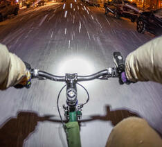 Person cykler udenfor i snevejr med tændte cykellygter med batterier