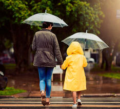 Voksen og barn går i regn med paraplyer