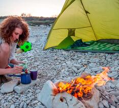 Kvinde laver instant kaffe på telttur over bål.