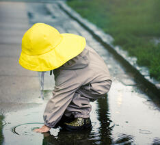 barn i regntøj og gul regnhat leger i vandpyt