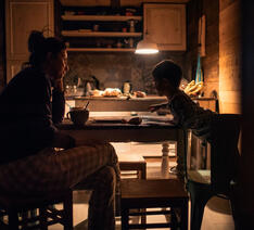 Mor og barn i køkkenet ved spisebordet i næsten mørke