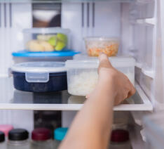 hånd rækker ind i køleskab med madrester i forskellige plastikbøtter