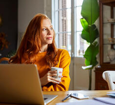 Kvinde ved sin computer kigger ud ad vinduet