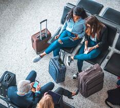Gruppe af mennesker der sidder med deres bagage og venter i en lufthavn.
