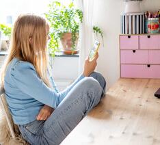 Teenagepige sidder på værelse og kigger på smartphone