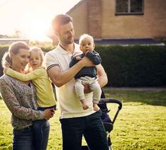 Kvinde og mand med to børn står i haven og kigger på deres nye hus