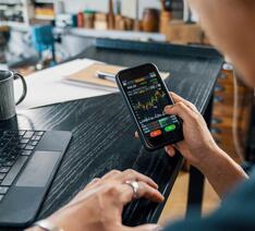 Mand med telefon og computer kigger på investeringer og aktiesparekonti