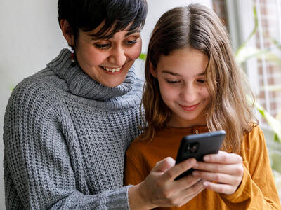 mor og datter står og kigger på smartphone, de skal beskytte datterens telefonnummer for telefonsalg